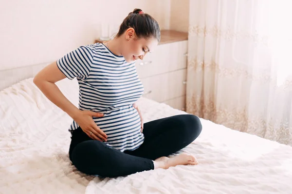 Hamilelik, dinlenme, insanlar ve beklenti konsepti mutlu hamile bir kadın yatakta oturup karnına dokunuyor.