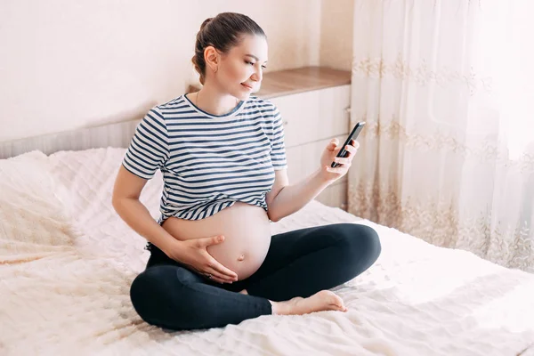 人と期待のコンセプト 彼女の寝室で携帯電話を使用して 自宅のベッドでスマート フォンで妊婦のクローズ アップ — ストック写真