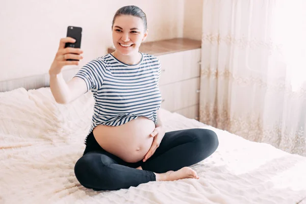 妊娠中の女性は Selfie を作るします 幸せそうに見えて彼女のスマート フォンでセルフ ポートレートを作るを見越して美しい女性 — ストック写真