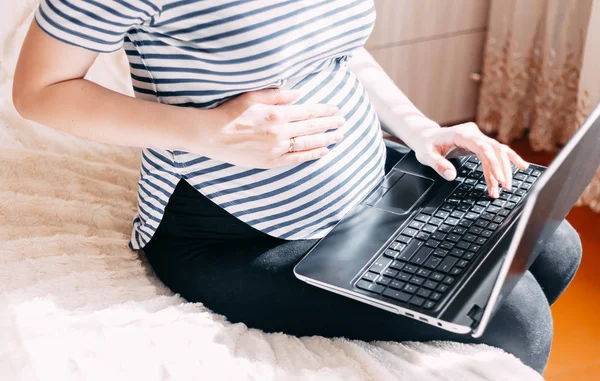 妊娠中の女性のラップトップに取り組んでいます 彼女の仕事場を自宅で座っている間ノート パソコンに何かを入力する妊娠中の実業家の画像をトリミング — ストック写真