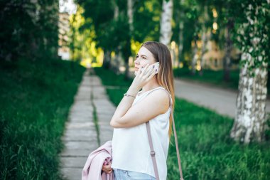 Cep telefonu, açık kullanarak koyu saçlı güzel genç kız. Telefonda konuşurken bir yaz parkta rahat genç bayan portresi.
