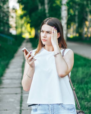 El, bir cep telefonu ile parkta yürüyen genç güzel kadın baş ağrısı vardır ve Smartphone'da baktığımızda, beyaz tişört ve uzun saç