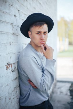 Genç yakışıklı adam gri kazak ve siyah şapka, beyaz tuğla duvara yakın duran genç çocuk model