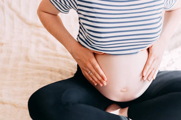 シャツで妊娠中の女性は ウィンドウに対して自宅で白い背景の上の腹に手を保持します 出産準備 期待のコンセプトです クローズ アップ コピー スペース 屋内で 妊娠の美しい柔らかい雰囲気写真 — ストック写真