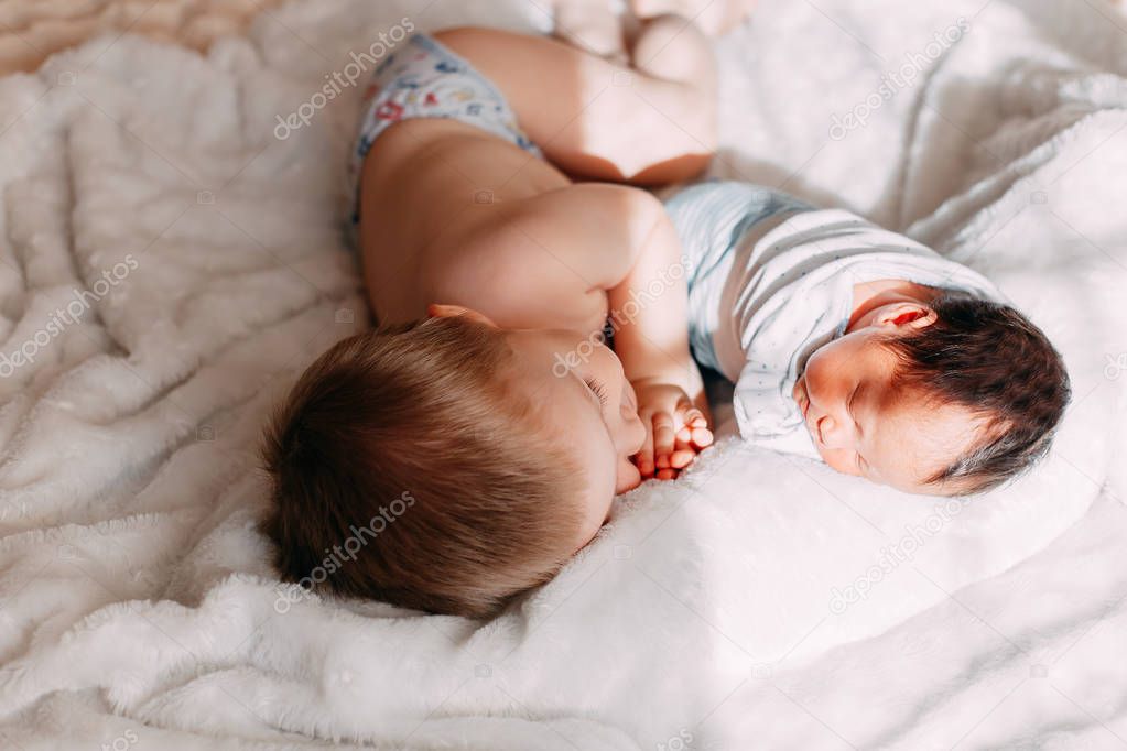 Happy little brother with newborn baby lying in a bed together, kissing and hugging. Siblings. New born baby and three years old brother together. Love. Family.