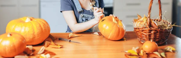 Woman hands drawing scary face on pumpkin with a black marker pen on home background for Halloween. Holiday decoration concept. long banner