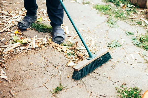 Man is cleaning and sweeping the floor with a green broom. Repairing maintenance works outdoors.