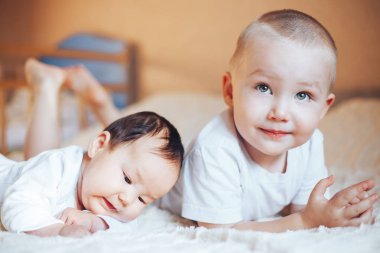 siyah saçlı küçük bacım ile evde yatakta oynayan çocuklar beyaz giysili ağabeyi sarışın çocuk evlat