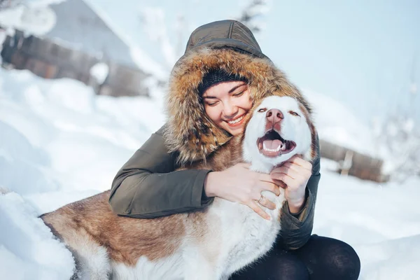 若い女性は 青い目を持つ赤い犬ハスキーと遊ぶ 庭の雪の朝 暖かい服に身を包んだ女の子 — ストック写真