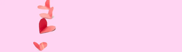 Línea vertical de corazones de papel rojo forma aislada sobre fondo rosa enfoque seleccionado enfoque suave bandera larga — Foto de Stock