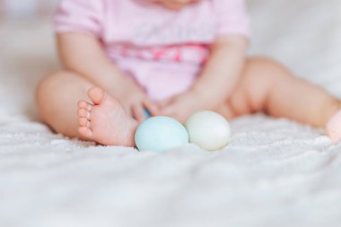 Oturma odası, mutlu bir şekilde gülümseyerek babygirl yatakta oturup pembe giysiler içinde renkli Paskalya yumurtaları ile oynarken, sevimli küçük bebek kız