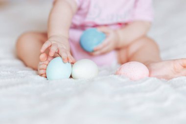 Oturma odası, mutlu bir şekilde gülümseyerek babygirl yatakta oturup pembe giysiler içinde renkli Paskalya yumurtaları ile oynarken, sevimli küçük bebek kız