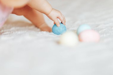 Oturma odası, mutlu bir şekilde gülümseyerek babygirl yatakta oturup pembe giysiler içinde renkli Paskalya yumurtaları ile oynarken, sevimli küçük bebek kız