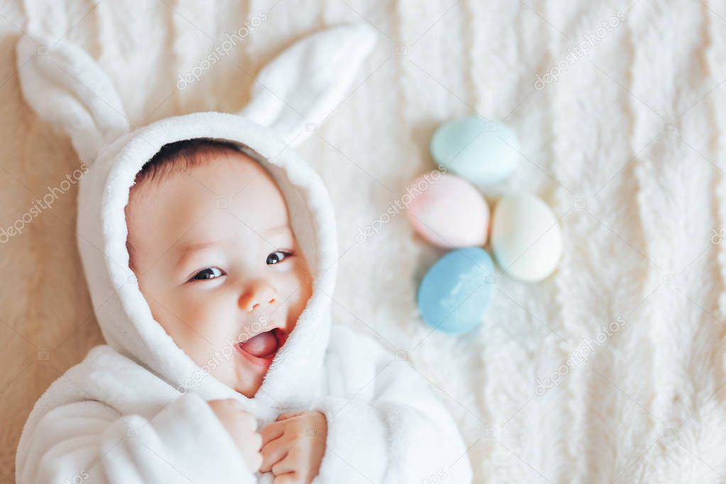 small cute child smiling happy baby in a white bunny rabbit costume easter playing with colorful easter eggs wanted to eat them top view