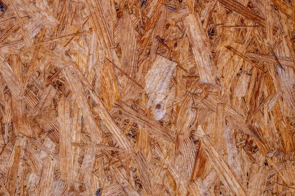 Las placas OSB están hechas de astillas de madera marrón lijadas en un fondo de madera. Vista superior del fondo de chapa de madera OSB, superficies estrechas y sin costuras —  Fotos de Stock