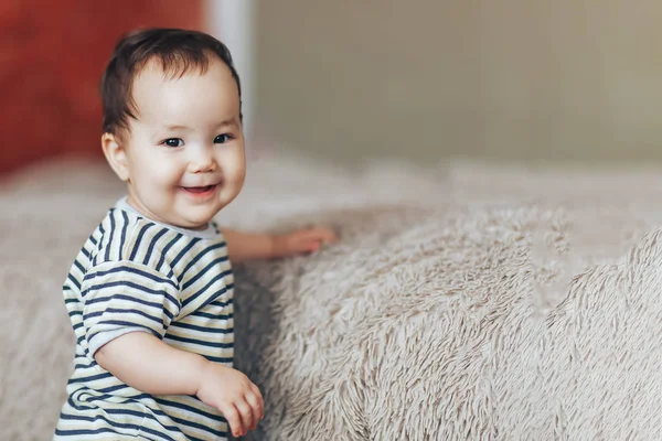 Ładny toddler chłopiec lub dziewczynka stojącego obok łóżka, uśmiechając się i patrząc na kamery w mieszkaniu — Zdjęcie stockowe