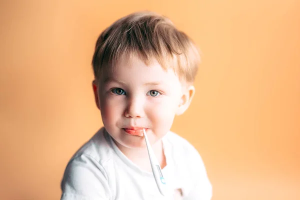 Άρρωστο παιδί με ένα θερμόμετρο στο στόμα του με θλιμμένο πρόσωπο σε πορτοκαλί φόντο — Φωτογραφία Αρχείου