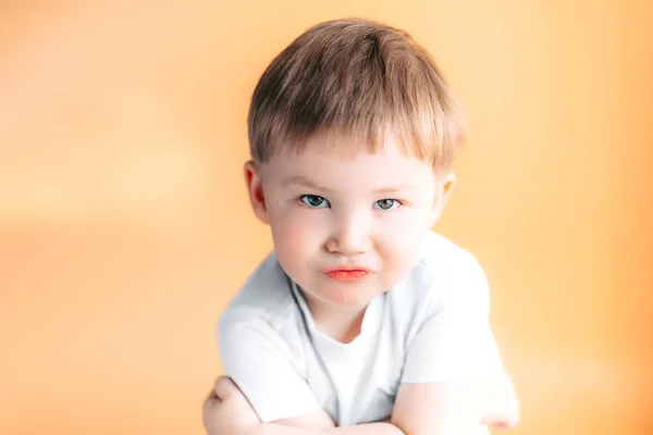 Πορτραίτο closeup ενός θυμωμένος αγόρι με τα χέρια του διπλωμένα σε πορτοκαλί φόντο — Φωτογραφία Αρχείου