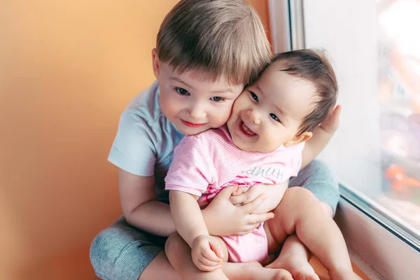 elder brother hugging his baby sister playing and smiling together. family concept love protect