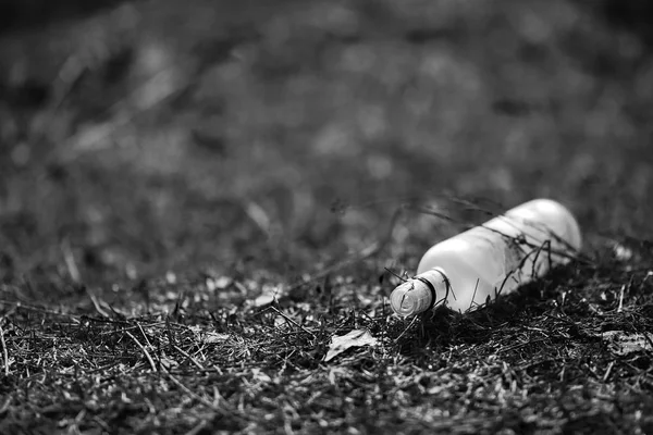 Empty white glass bottle lying on grass in early spring, polluted, conservancy. rubbish after last snows of winter black and white picture — Stock Photo, Image