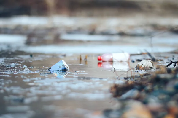 Verlaten lege Roze plastic fles en blauw kan vuilnis op de oever van de riviermilieu vervuiling — Stockfoto