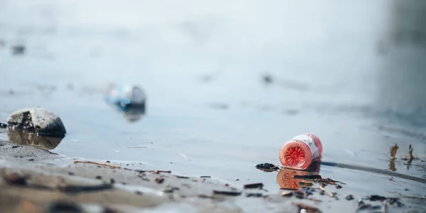 Porzucona pusta, różowa plastikowa butelka i niebieska może śmieci na brzegu rzecznego zanieczyszczenia — Zdjęcie stockowe