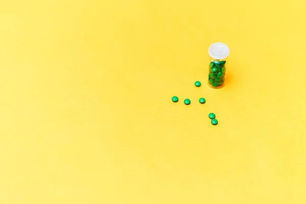 Medische groene pillen in een glazen fles op gele achtergrond copyspace, gezondheid — Stockfoto