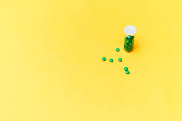 Pílulas medicinais verdes em uma garrafa de vidro em fundo amarelo copyspace, saúde — Fotografia de Stock