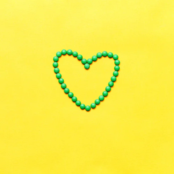 Píldoras redondas verdes comprimidos en forma de corazón sobre fondo amarillento — Foto de Stock