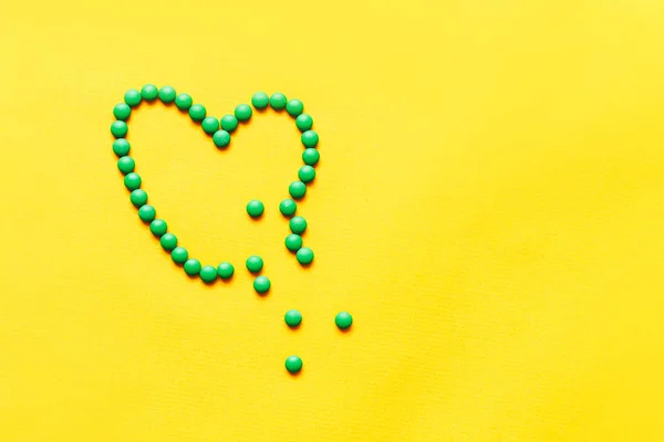 Yeşil yuvarlak haplar tabletler yuellow arka plan üzerinde kalp şekli brocken — Stok fotoğraf