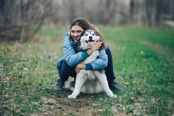 Mujer joven jugar con perro husky para un paseo en el bosque de primavera. riendo divirtiéndose, feliz con la mascota —  Fotos de Stock