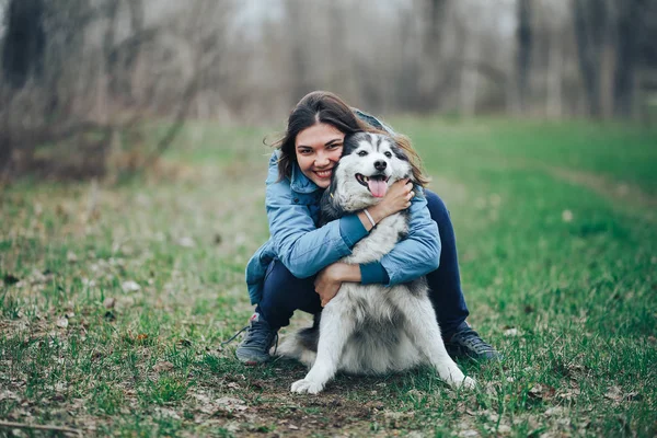 Mujer joven jugar con perro husky para un paseo en el bosque de primavera. riendo divirtiéndose, feliz con la mascota —  Fotos de Stock