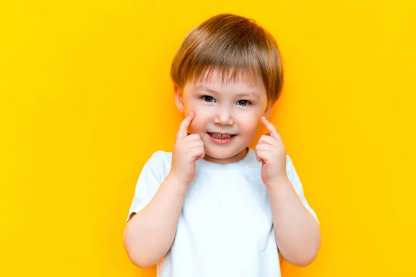 Πορτραίτο του εύθυμου μικρού αγοριού τριών ετών, που στέκεται απομονωμένο σε κίτρινο φόντο. Κοιτάζω την κάμερα. δείχνοντας λευκά δόντια, χαμογελαστά — Φωτογραφία Αρχείου