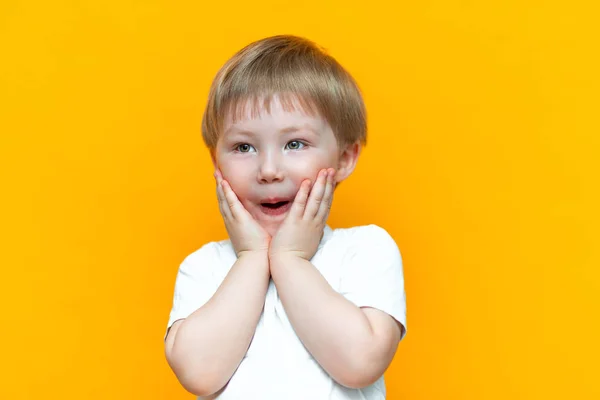 Χαρούμενο μωρό αγόρι τριών ετών σε λευκό t-shirt στέκεται σε κίτρινο φόντο, άνοιξε το στόμα του έκπληκτος, ξανθιά μαλλιά μικτός αγώνας Ασίας — Φωτογραφία Αρχείου
