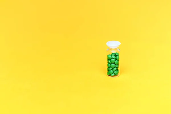 Pílulas medicinais verdes em uma garrafa de vidro em fundo amarelo copyspace, saúde — Fotografia de Stock