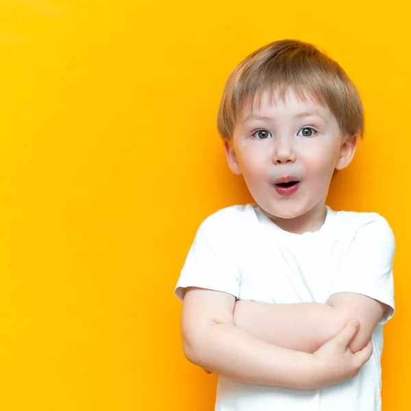 Cheerful baby boy three years old in white t-shirt stands on yellow background, open his mouth surprised, blonde hair mixed race asian — Stock Photo, Image