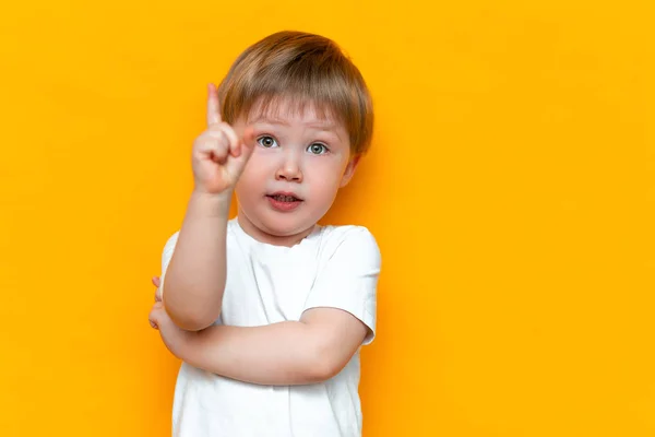 Portrait of cute handsome blonde little boy with finger pointed up. Little child has idea. Kid isolated on yellow blackground. Success, bright idea, creative ideas — Stock Photo, Image