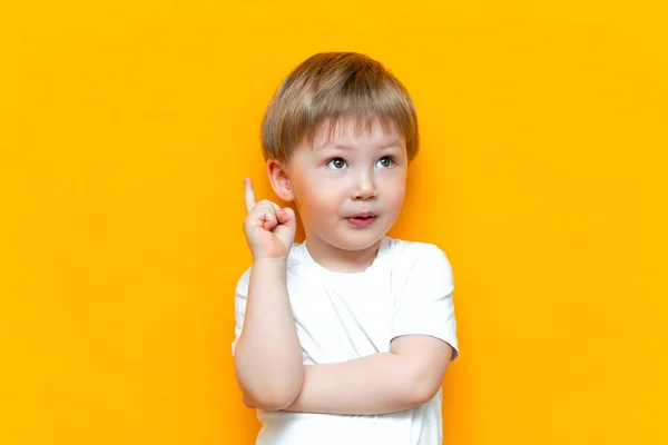 Retrato de lindo niño rubio guapo con el dedo hacia arriba. El niño tiene una idea. Un chico aislado en el suelo negro amarillo. Éxito, idea brillante, ideas creativas — Foto de Stock