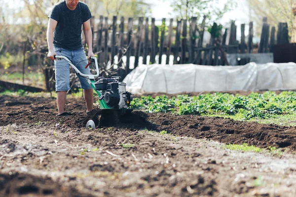 若い農家の庭師は、地面の土壌ローラー、耕運機、耕運機、栽培機を栽培し、作物、春を植える準備をします。現代の農業技術農業 — ストック写真