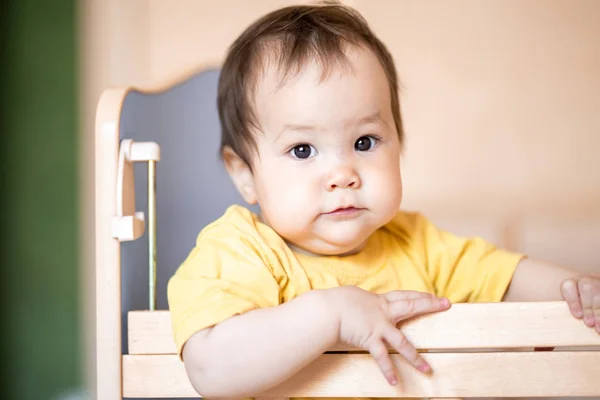 Sarı t-shirt evde beşik ayakta koyu saçlı sevimli küçük kız bebek — Stok fotoğraf
