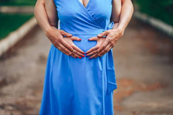 Mujer embarazada y su marido tomados de la mano en la barriga en forma de corazón. Joven familia amorosa. Nuevo concepto de vida — Foto de Stock