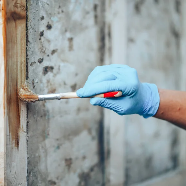 Mano sosteniendo un pincel aplicando pintura de barniz en una puerta de madera —  Fotos de Stock