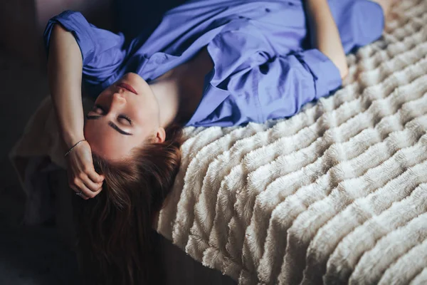 Sexy jovem mulher bonita com olhos grandes azuis cabelo lond deitado na cama em casa em camisa azul — Fotografia de Stock