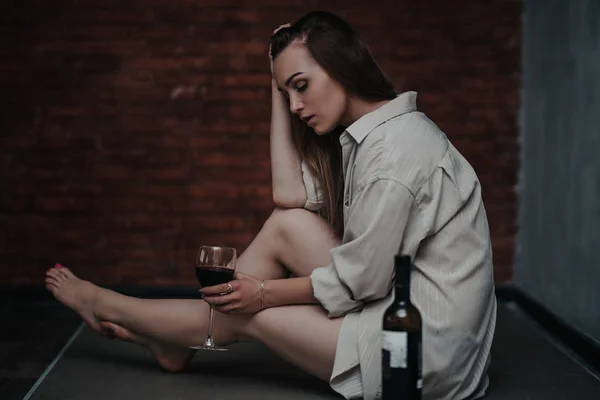 Красивая грустная женщина сидит на полу в рубашке, держать вино она расстроена, одна, никто не любил, без любви — стоковое фото