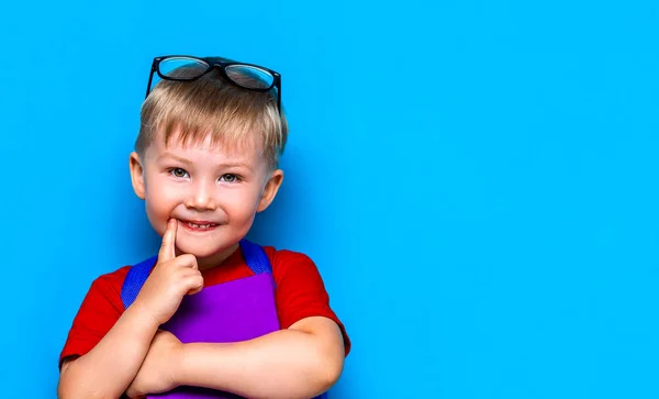 彼の頭の上に眼鏡をかけて小さな幸せな笑顔の少年、手に本、彼の肩にスクールバッグ。学校に戻る学校に行く準備ができている — ストック写真