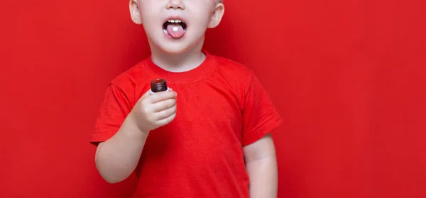 Μικρό τρία χρόνια αγόρι θέλει να φάει χάπι, δισκίο στη γλώσσα του, μπορεί να μπουκάλι στο χέρι. κόκκινο φόντο — Φωτογραφία Αρχείου