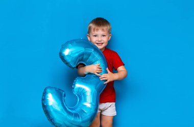 mavi arka plan üzerinde küçük sevimli sarışın çocuk folyo kaplı küre baloon mavi renk tutarak. mutlu yıllar üç yaşında