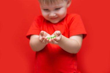 küçük üzgün çocuk çocuk elinde hap bir sürü tutun. kırmızı t-shirt, kırmızı arka plan tehlikeli kavram, tablet ve bebek