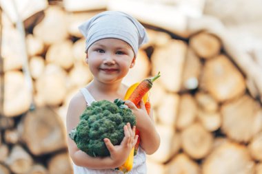 litle mutlu beyaz tulum ve gri saç bandı elinde taze organik sebze tutan çiftçi çocuk gülümseyen çocuk. bahçe, hasat sezonu