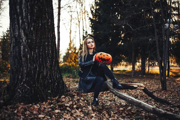 Hermosa bruja moderna sosteniendo calabaza de halloween en el bosque. Octubre. felices fiestas —  Fotos de Stock